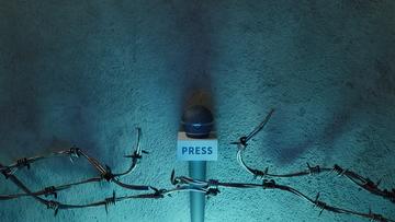 A reporter's microphone at a press conference, through barbed wire